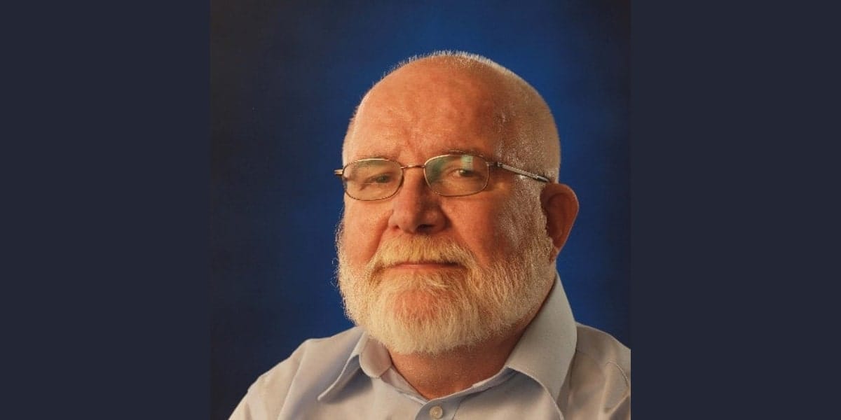 A bearded older man with glasses, reminiscent of Norm Peterson, is wearing a light blue shirt against a dark gradient, serving as a poignant tribute.